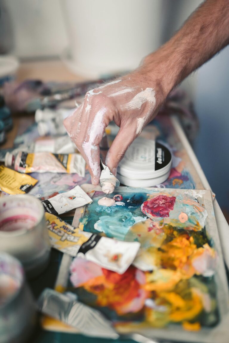 Close-up of hand mixing oil paints on a palette with paint tubes and brushes around.